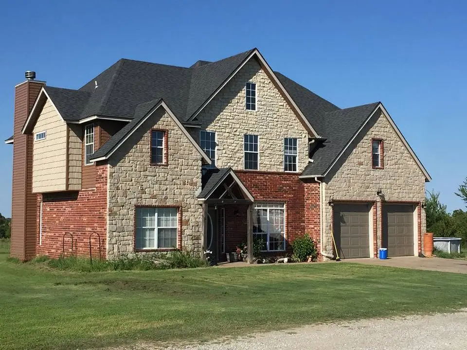 Two-story Rogers County home with stone, brick, and lap siding under a newly installed shingle roof by C&A Roofing & Construction